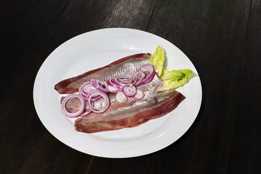 Matjesfilet ohne Haut mit Zwiebeln und Salatblatt auf Teller