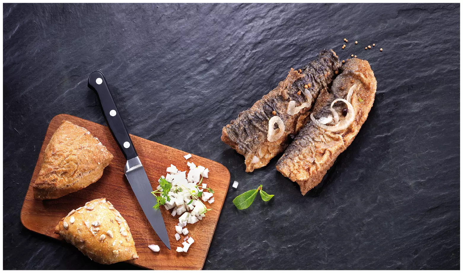 zwei Brathering-Filets mit Zwiebeln auf schwarzem Stein, Bro