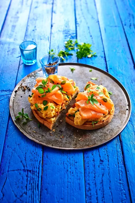 Brot mit Rührei, Räucherlachs und Kräutern auf Teller