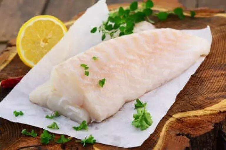 rohes Kabeljaufilet auf Backpapier mit Kräutern und Zitrone