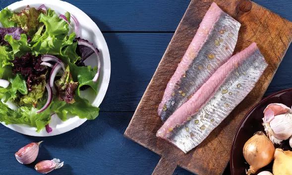 zwei rohe Heringfilets mit Haut auf Holzbrett neben Salat