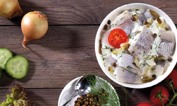 Heringsfilets in Sahnesoße mit Zwiebeln und Tomate serviert