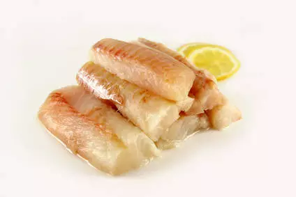 rohes Kabeljaufilet auf weißem Teller mit Zitronenscheibe