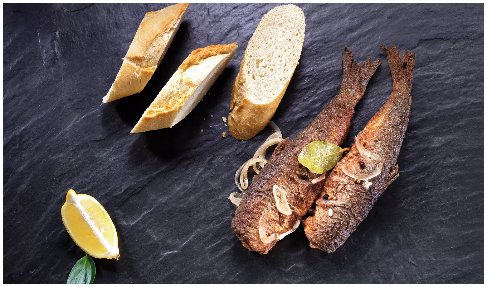Zwei gebratene Fische mit Brot und Zitronenspalte angerichte