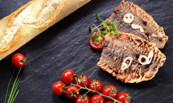 Gebratene Scholle mit Knoblauch, Baguette und Tomaten auf Sc