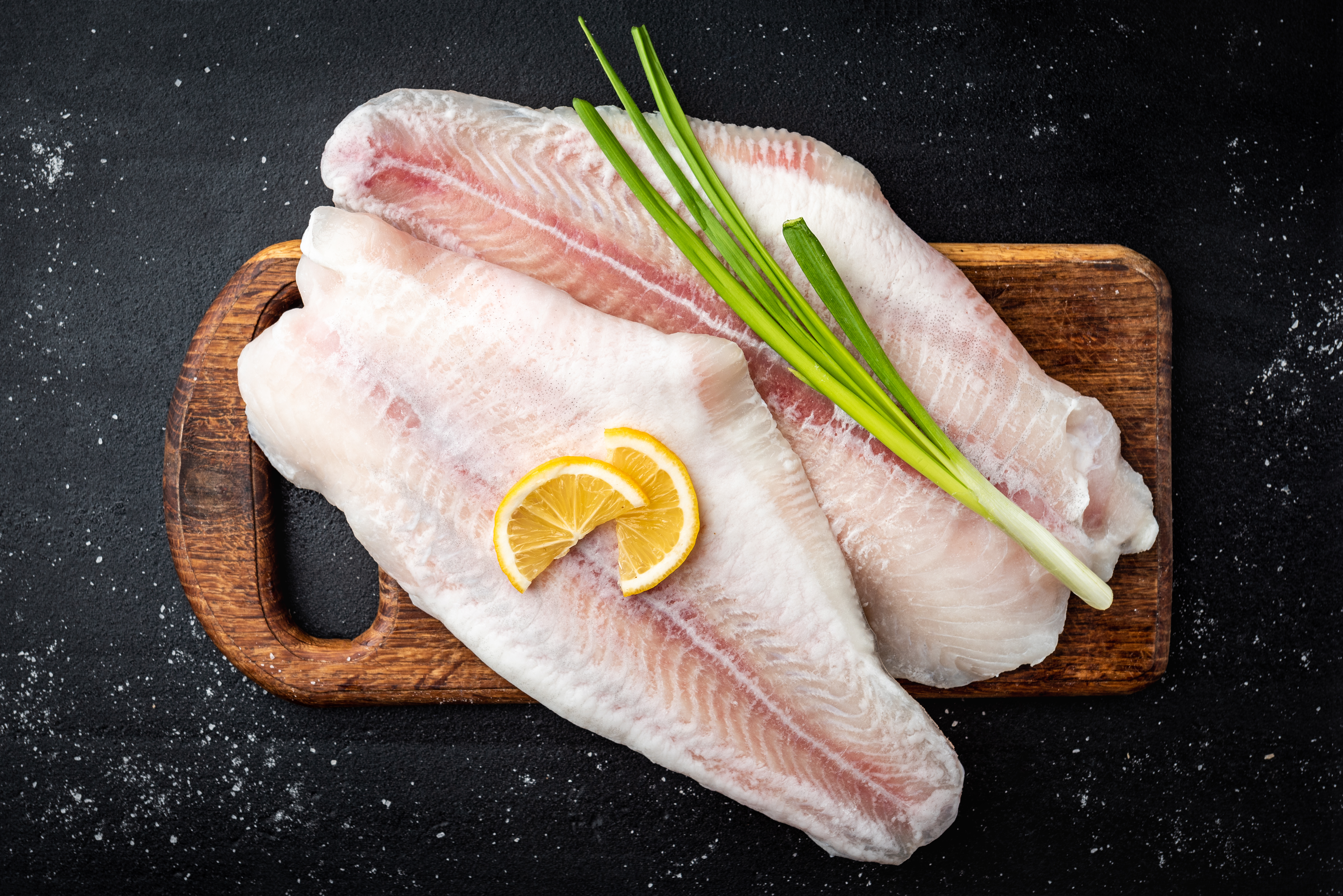 rohes Pangasiusfilet auf Holzbrett mit Zitrone und Lauchzwie