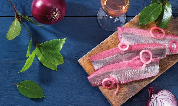 Matjesfilets mit roten Zwiebelringen auf Holzbrett