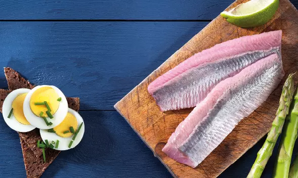 Zwei Matjesfilets auf Holzbrett mit Ei, Brot und Spargel