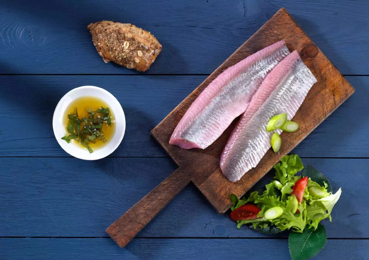 Rohe Heringsfilets auf Holzbrett mit Salat und Brot